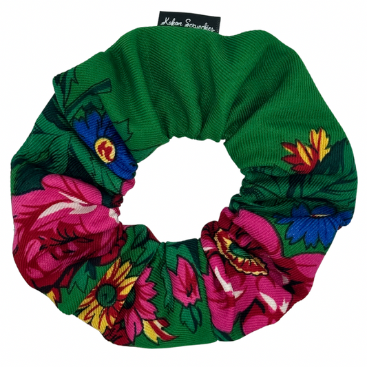 A green scrunchie with a floral pattern consisting of pink, yellow, and blue flowers.
