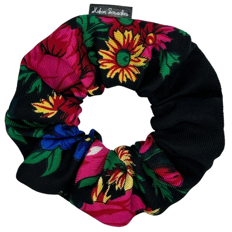 A black scrunchie with a vibrant floral pattern consisting of large flowers in red, pink, yellow, and blue on a tag, against a white background.