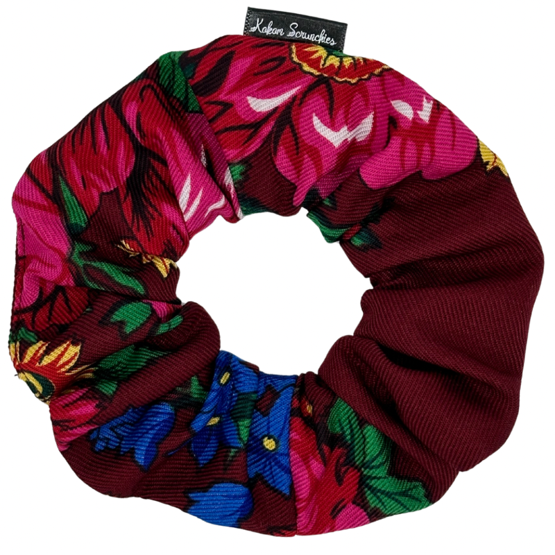 A burgundy hair scrunchie with a floral pattern, predominantly featuring pink, blue, and green colors.