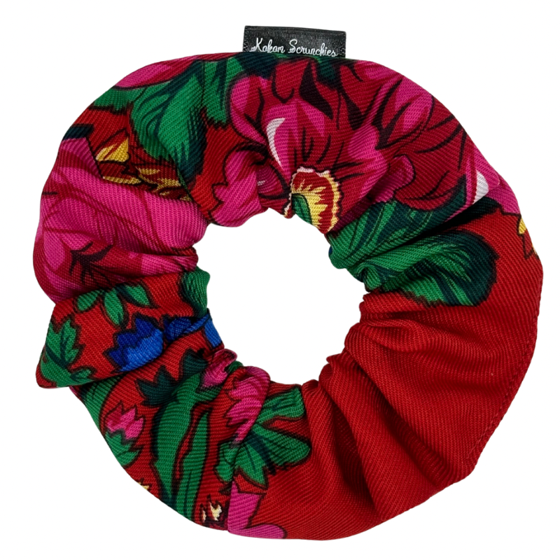 A red scrunchie with a floral pattern, featuring tags with brand name 'Kokom Scrunchies' visible.