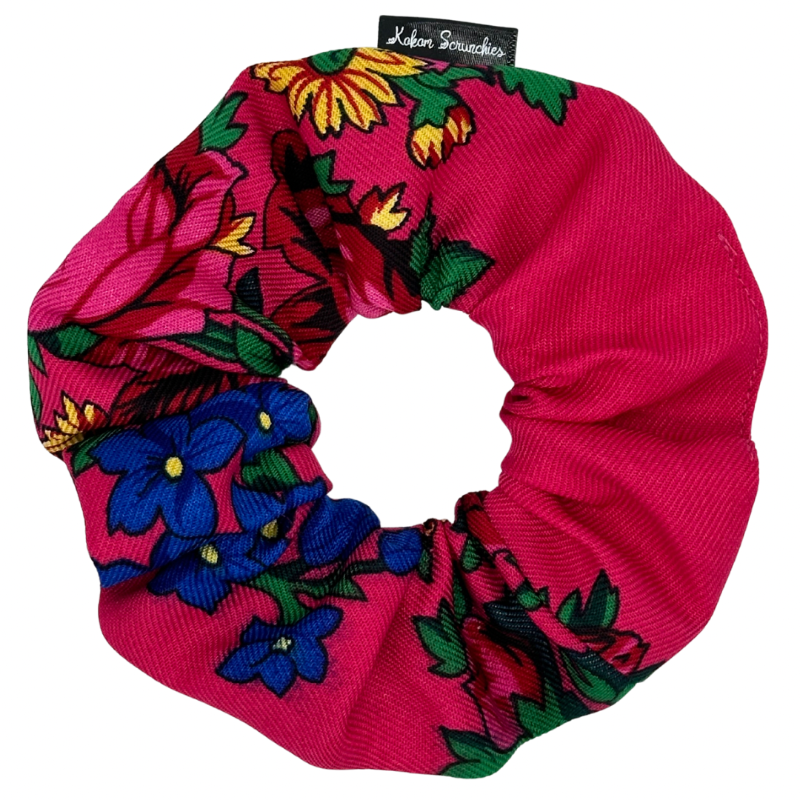 A pink hair scrunchie with a floral pattern, including blue and yellow flowers, and green leaves.