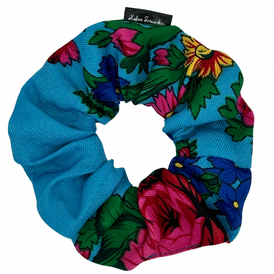 A light blue scrunchie with a floral pattern consisting of various flowers in different colors.